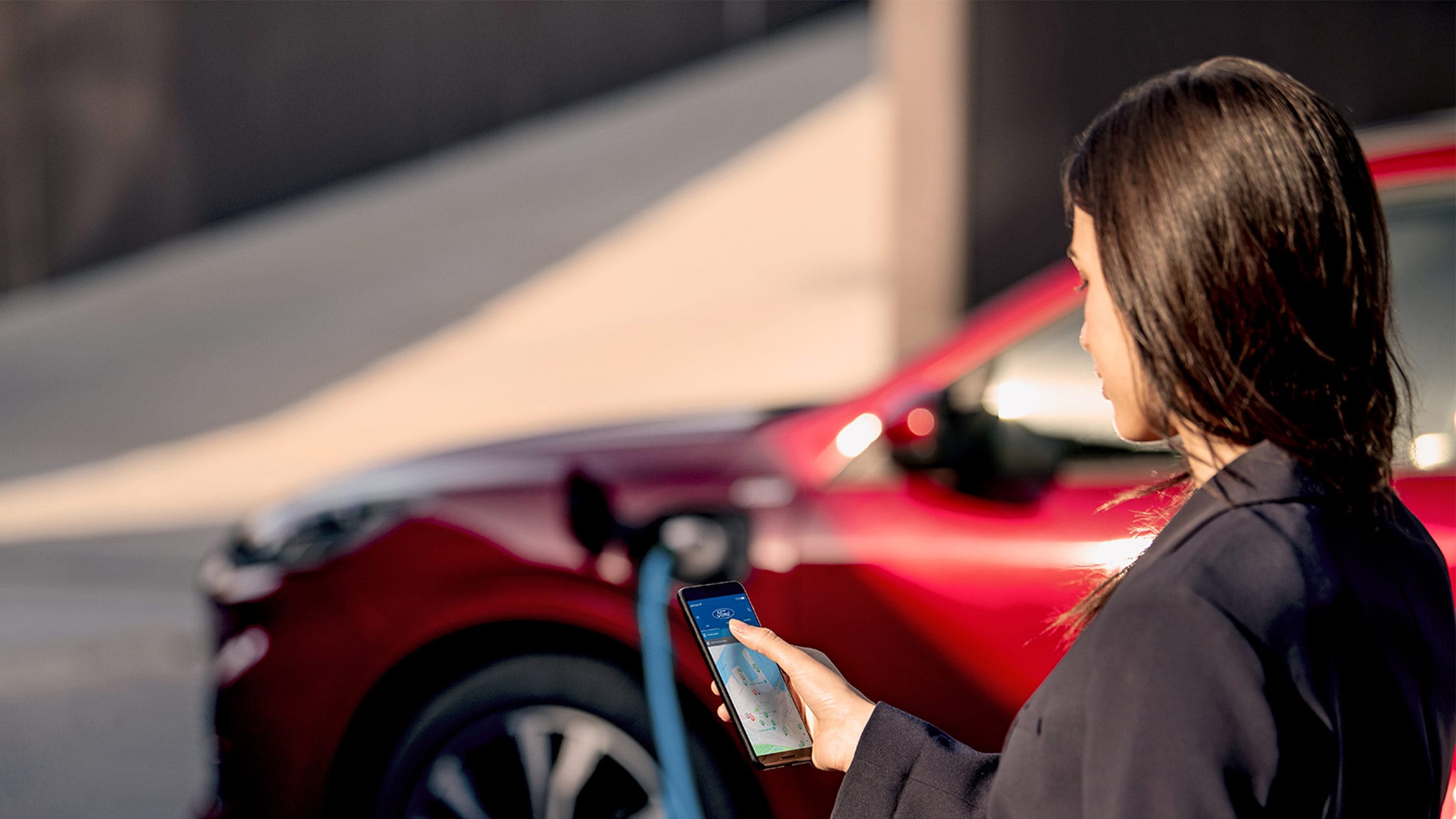 Une femme regarde son téléphone portable pendant qu’elle charge sa Ford
