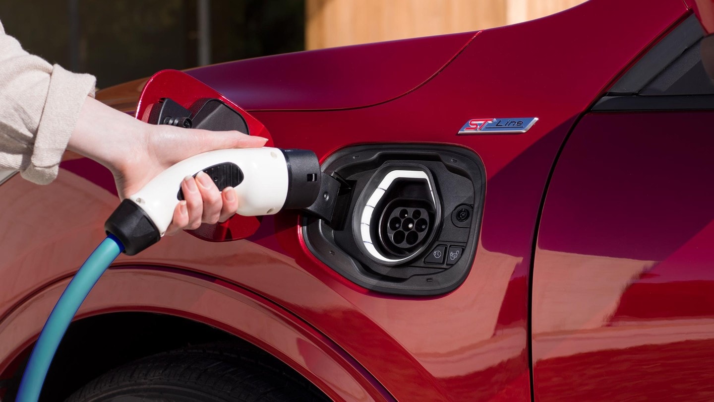Ford Kuga Plug-in Hybrid couleur rouge. Gros plan sur la prise de chargement. Une main tient la prise du câble de chargement