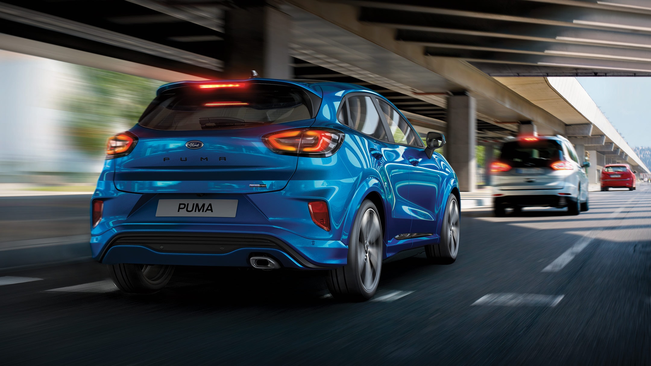 Ford Puma couleur bleue. Roulant sur une route avec les feux de freinage allumés, derrière une voiture grise