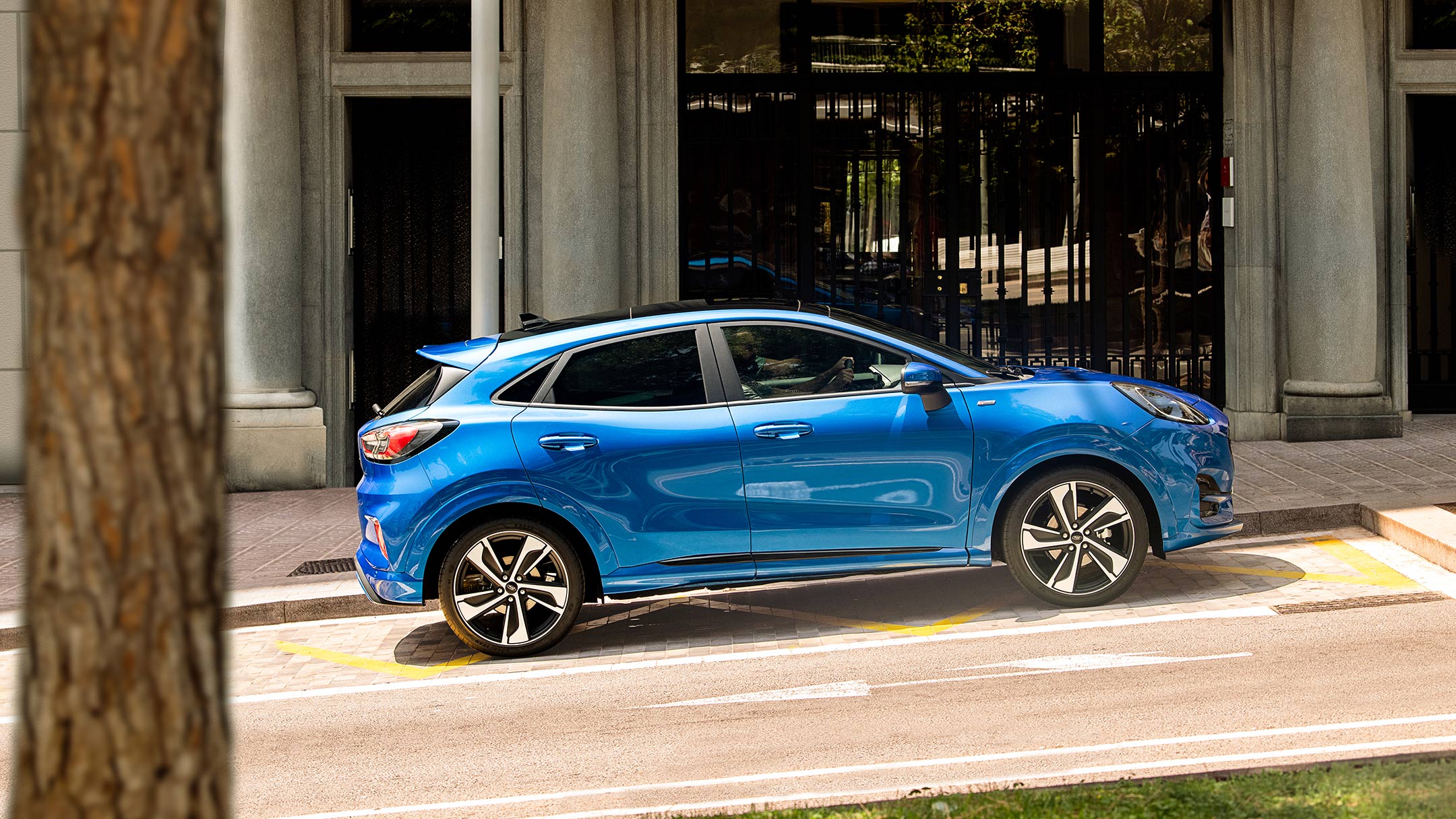 Ford Puma couleur bleue. Vue latérale dans une rue en pente, devant un restaurant