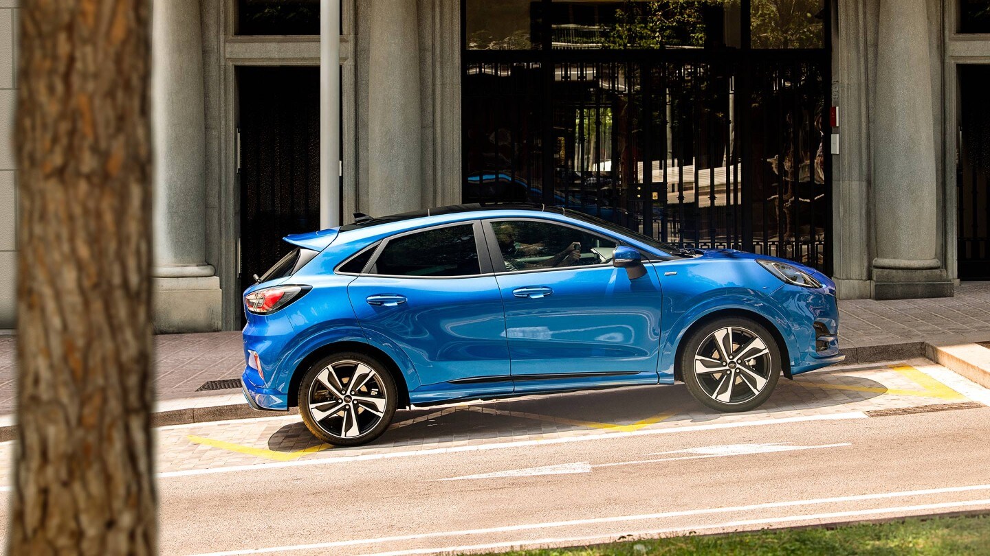 Ford Puma couleur bleue. Vue latérale dans une rue en pente, devant un restaurant