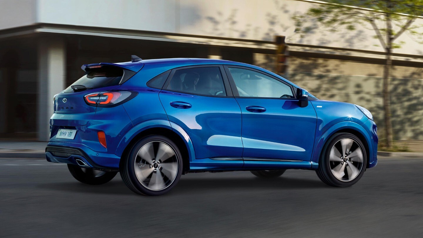 Ford Puma couleur bleue. Vue latérale, roulant devant une maison à l’arrière-plan