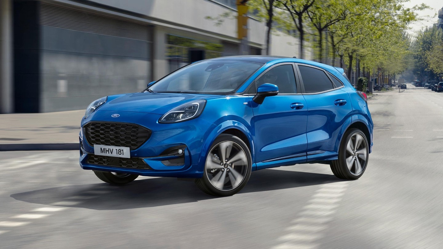 Ford Puma couleur bleue. Vue de trois quarts, roulant en ville à un carrefour devant des bâtiments historiques