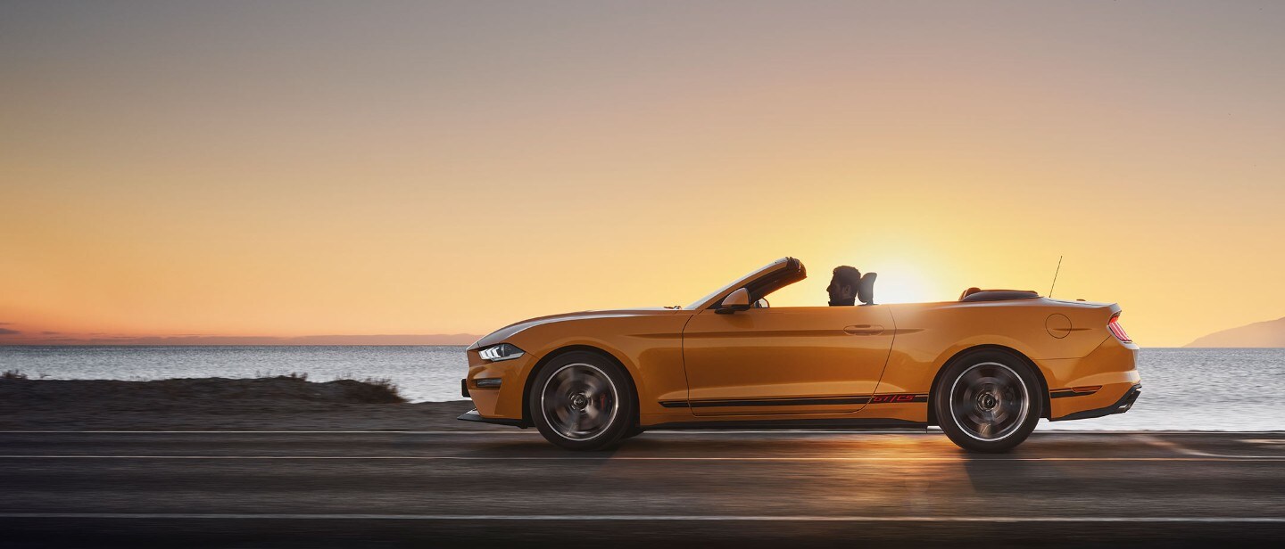 Ford Mustang California couleur orange. Vue latérale, roulant dans la nature au coucher du soleil.