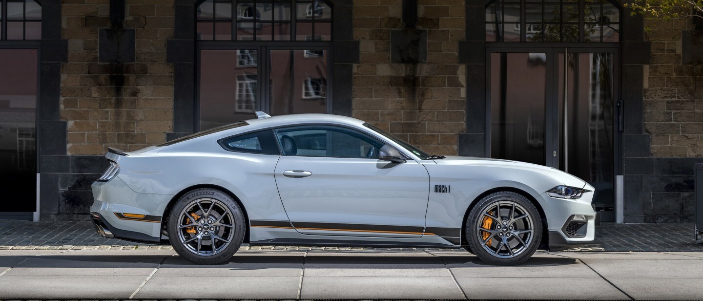 Ford Mustang Mach 1 couleur blanche. Vue latérale, garée devant un bâtiment moderne