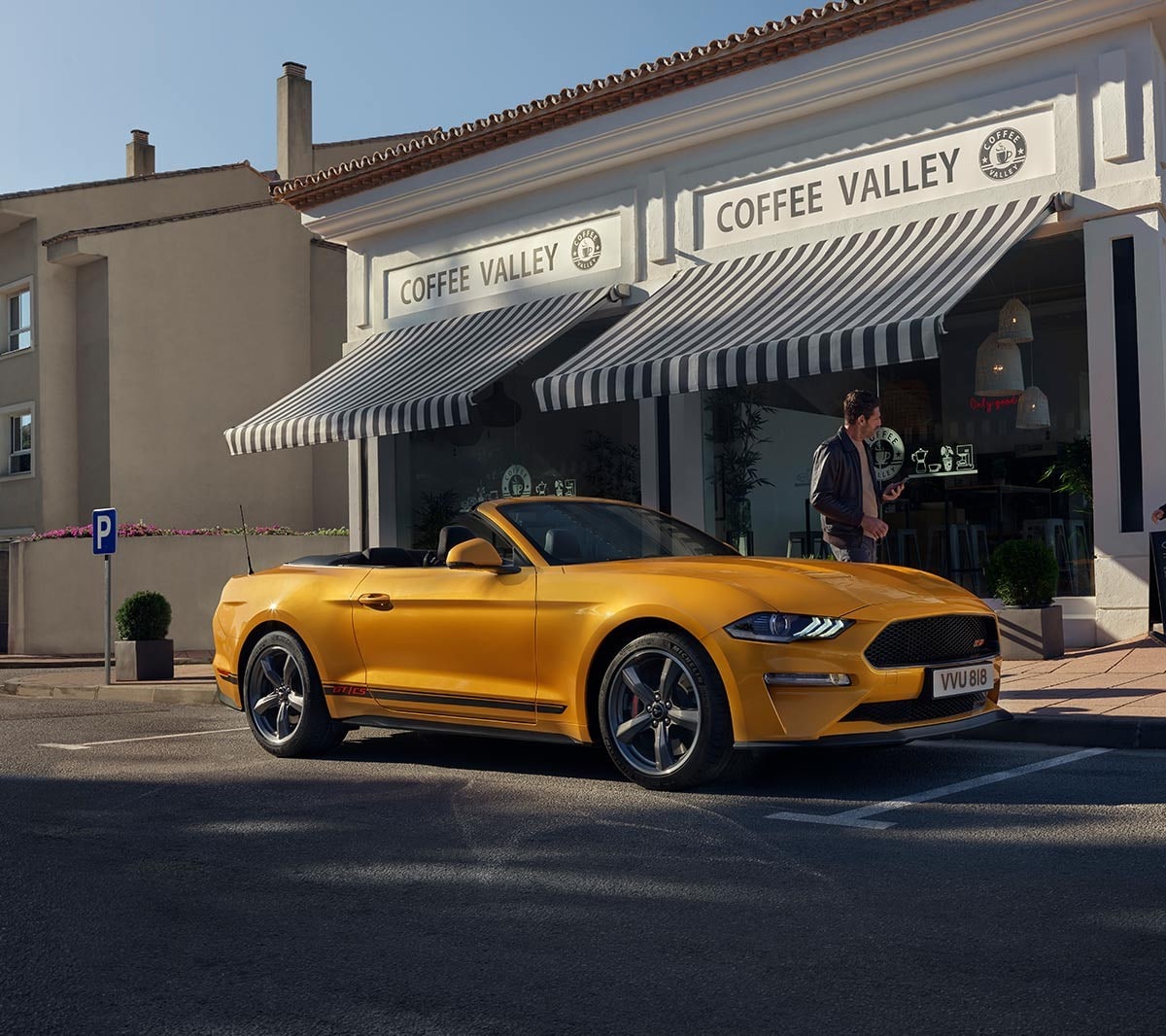 Ford Mustang California couleur orange. Vue de face aux trois quarts, stationnant devant un magasin.