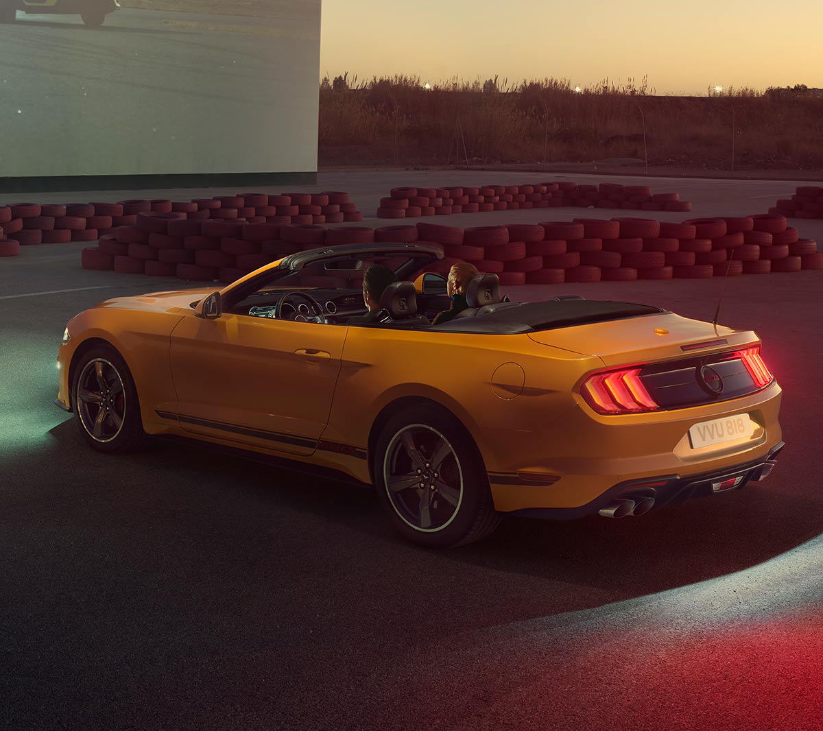 Ford Mustang California couleur orange. Vue arrière aux trois quarts, stationnant devant un bâtiment moderne.
