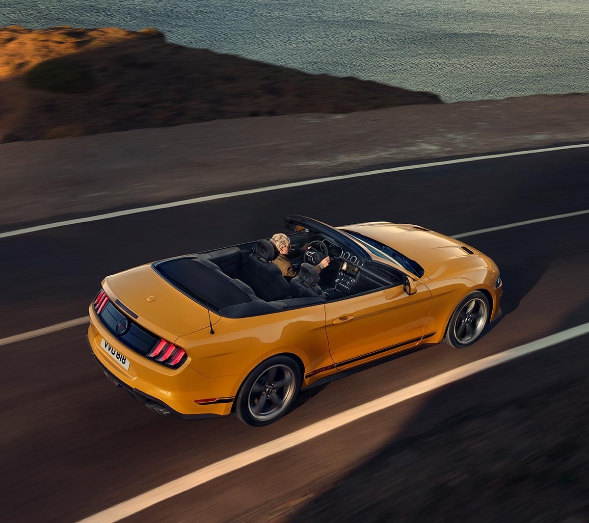 Ford Mustang California couleur orange. Vue arrière aux trois quarts, roulant sur une route.