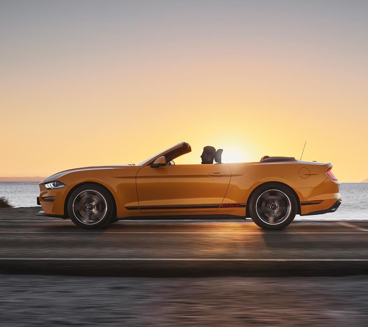 Ford Mustang California couleur orange. Vue latérale, roulant dans la nature au coucher du soleil.
