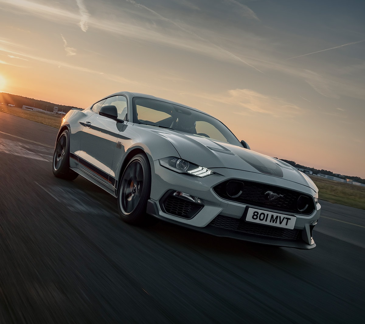 Ford Mustang Mach 1 couleur blanche. Vue de face aux trois quarts, roulant au coucher du soleil