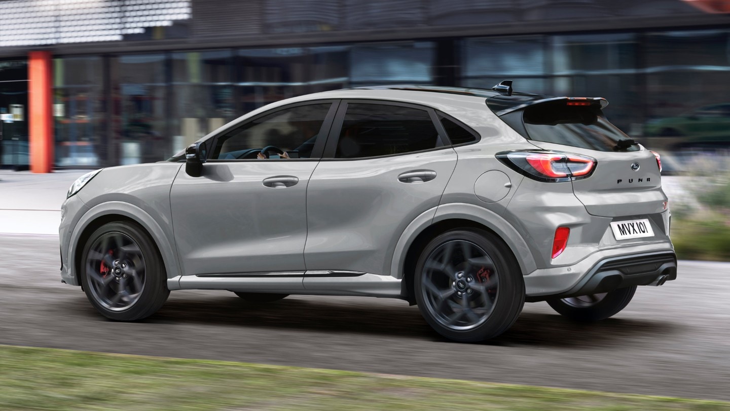 Ford Puma ST couleur grise, vue arrière aux trois quarts, roulant dans une rue devant un bâtiment moderne