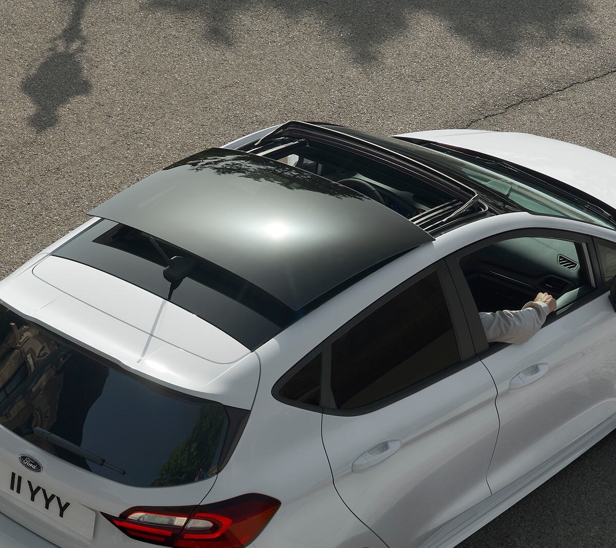 Ford Fiesta couleur blanche. Vue arrière aux trois quarts d’en haut, avec vue sur le toit ouvrant panoramique, roulant sur une route.