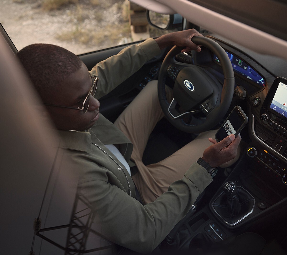 Ford Fiesta. Vue intérieure. Un homme assis sur le siège conducteur regarde son smartphone.