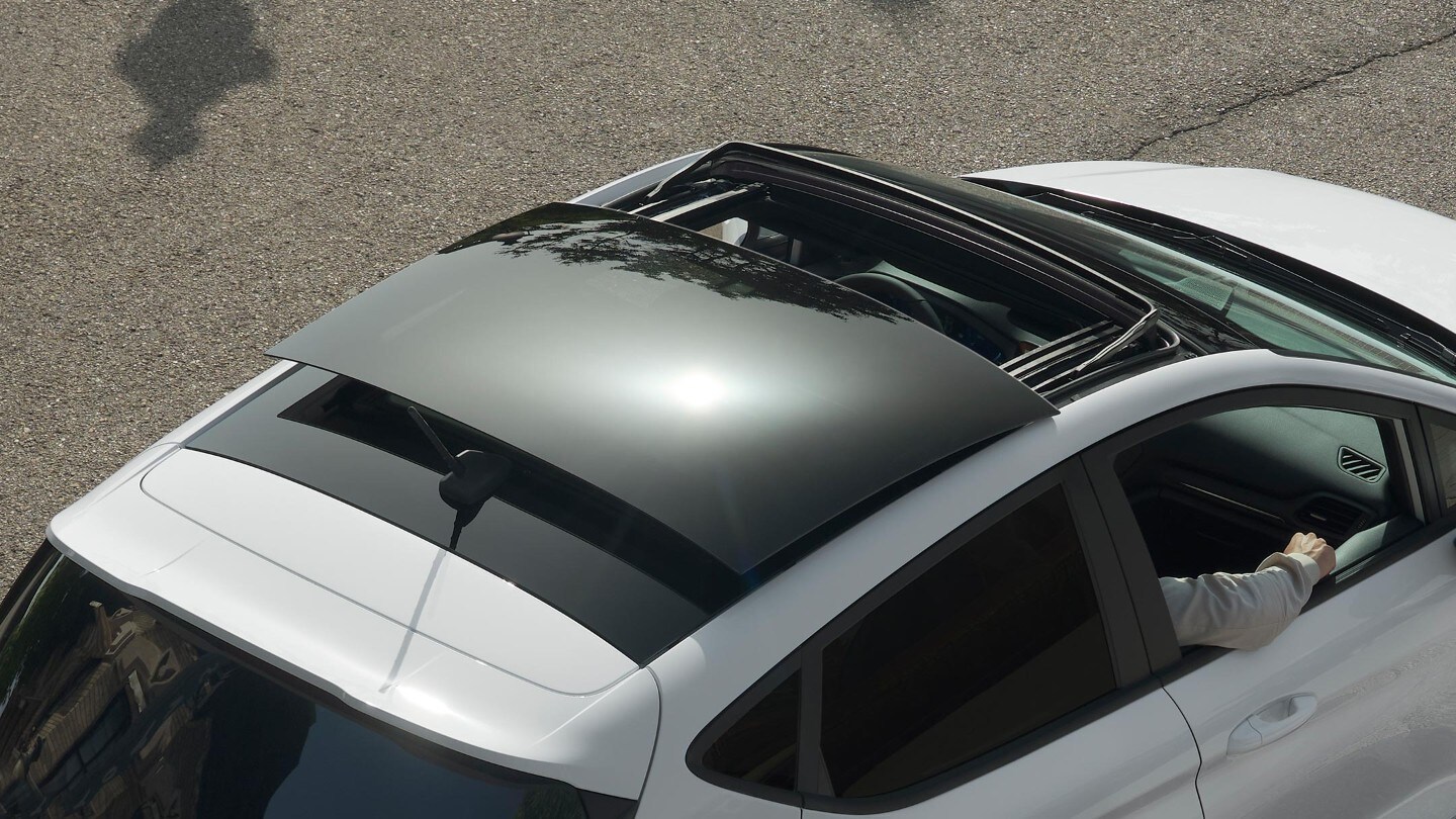 Ford Fiesta couleur blanche. Vue arrière aérienne aux trois quarts, avec vue sur le toit ouvrant panoramique, roulant sur une route.