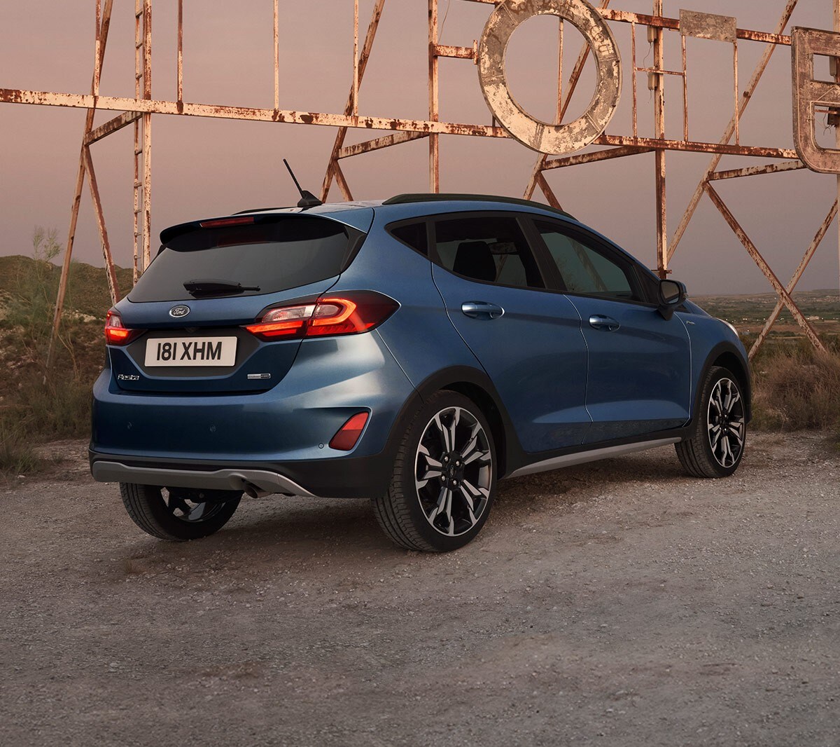 Ford Fiesta couleur bleue. Vue arrière aux trois quarts, stationnant sur un chemin de gravier.