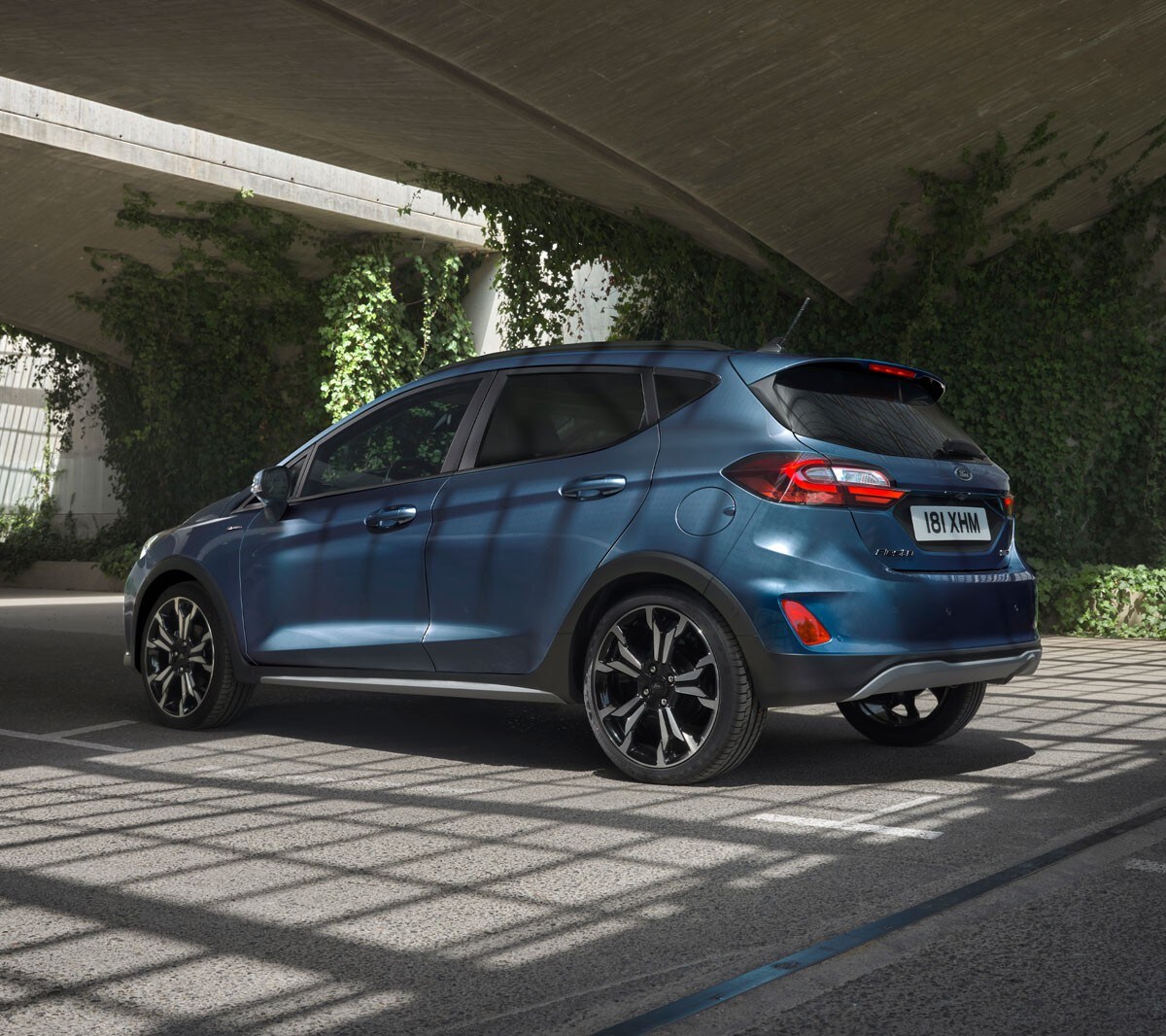 Ford Fiesta couleur bleue. Vue arrière aux trois quarts, passant sous une série de ponts.