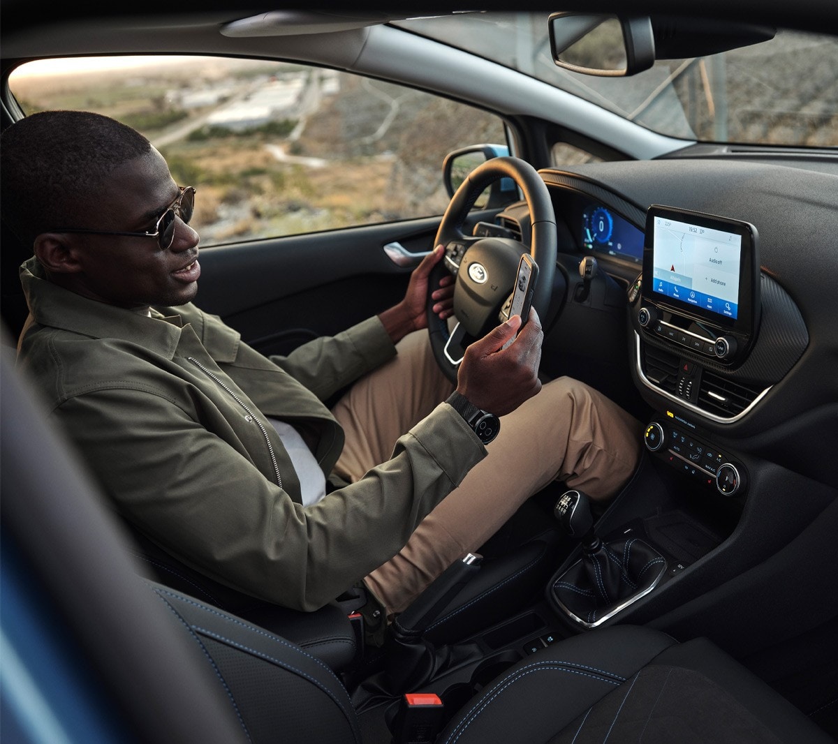 Ford Fiesta. Vue intérieure. Un homme assis sur le siège conducteur regarde son smartphone.