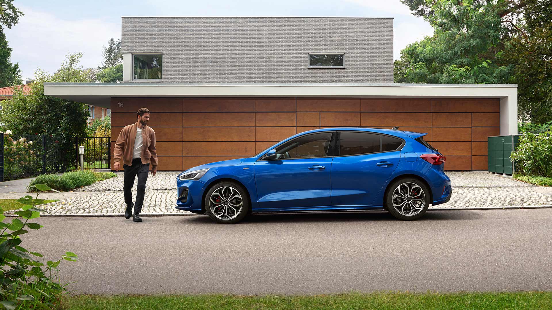 Un homme s’approche d’une Ford Focus de couleur bleue garée devant une maison.