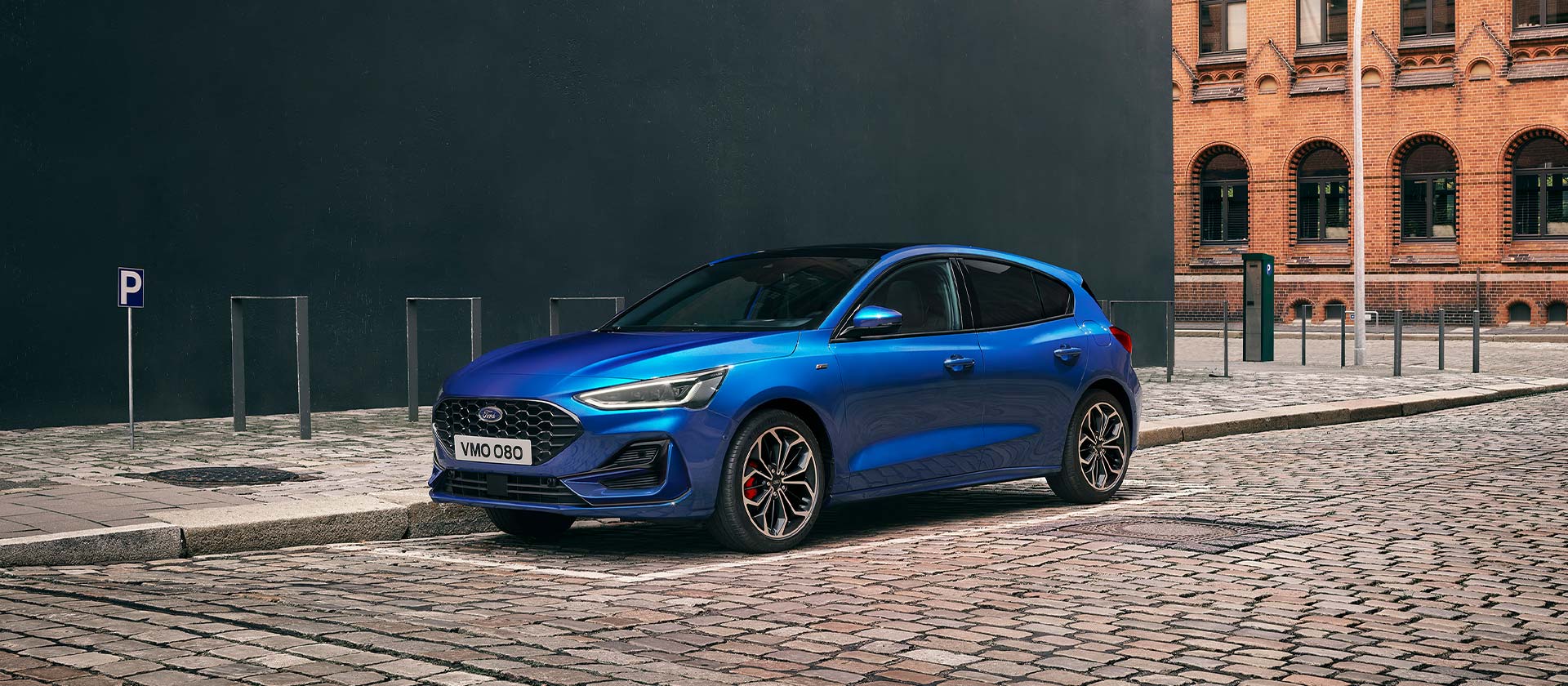 Une Ford Focus à hayon de couleur bleue est garée sur une route pavée dans un environnement urbain.
