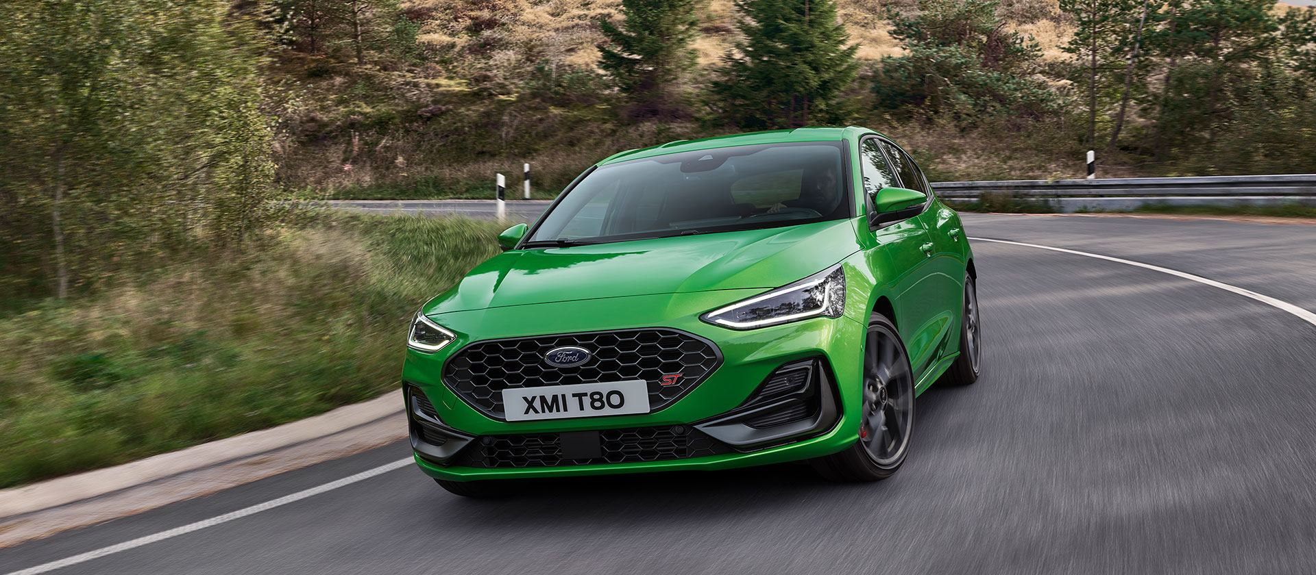 Une Ford Focus ST de couleur Mean Green négocie un virage sur une route pittoresque.