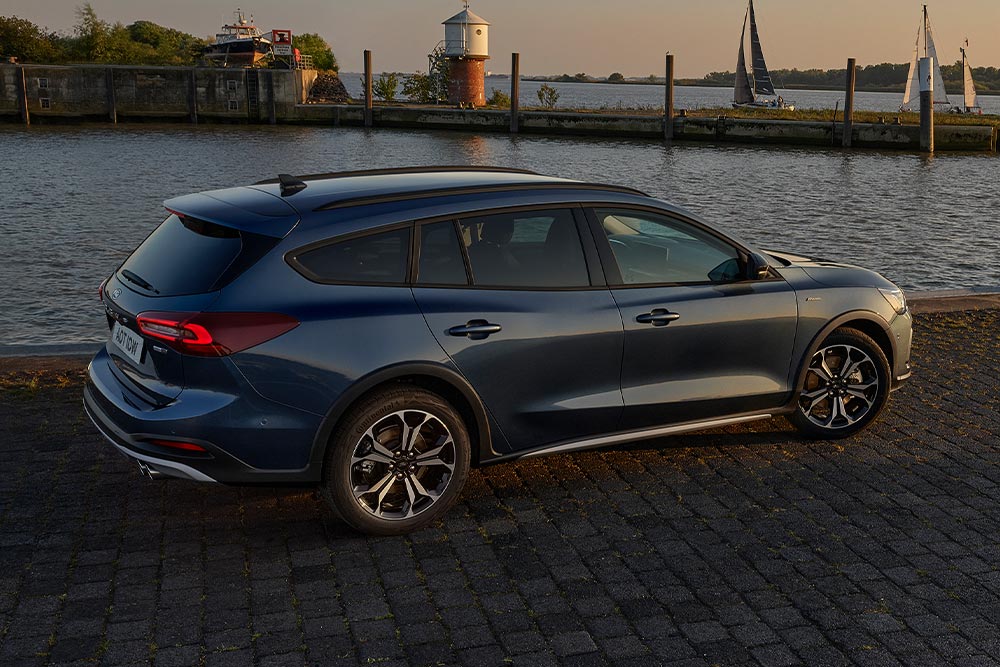 Une Ford Focus Active Turnier de couleur bleu foncé, garée près d’un plan d’eau au crépuscule.