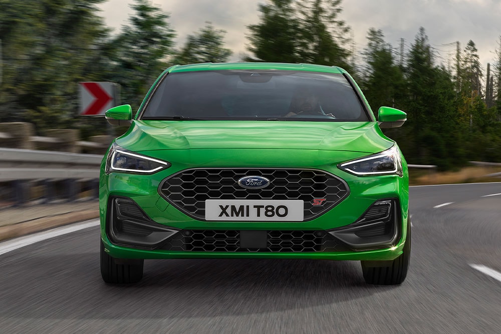 L’avant d’une Ford Focus ST de couleur Mean Green prenant un virage, avec des arbres flous à l’arrière-plan.