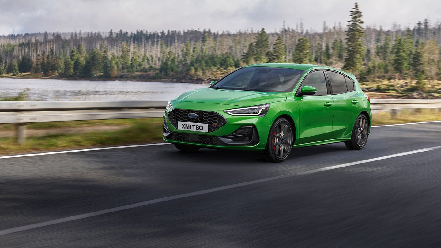 Une Ford Focus ST de couleur «Mean Green» roule sur une route, avec des arbres à l’arrière-plan.