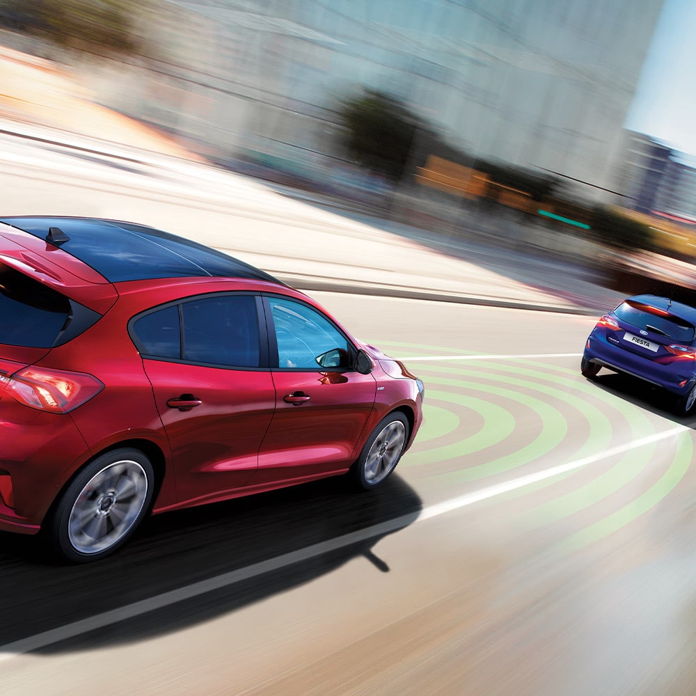 Un graphique montre une Ford Focus rouge dont les capteurs (représentés par des lignes bleues) détectent le véhicule qui précède avant d’activer le système de freinage d’urgence.