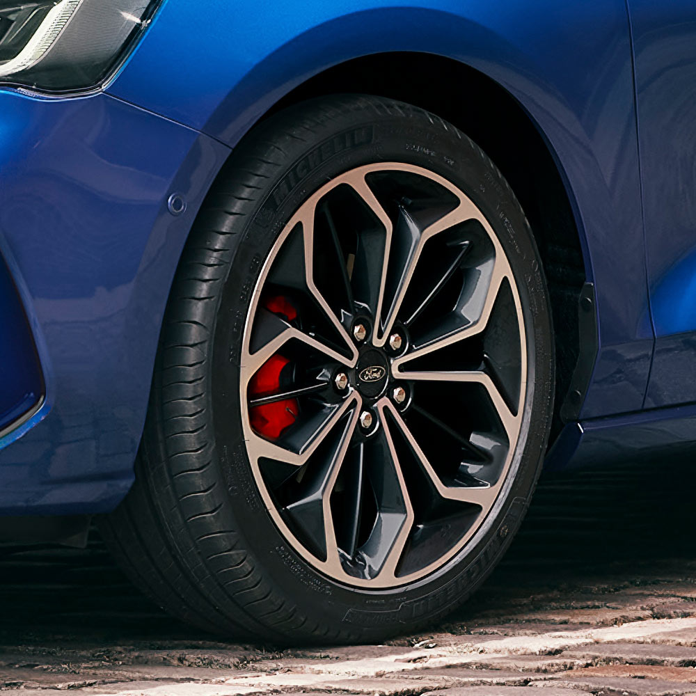 Gros plan sur les jantes en alliage grises avec étriers de frein rouges sur une Ford Focus de couleur bleue.