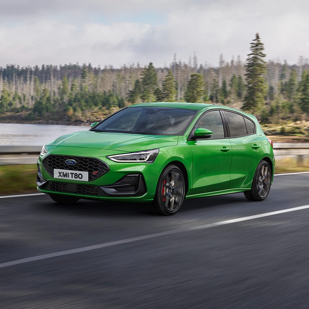 Une Ford Focus ST de couleur Mean Green roule sur une route sinueuse bordée d’arbres.