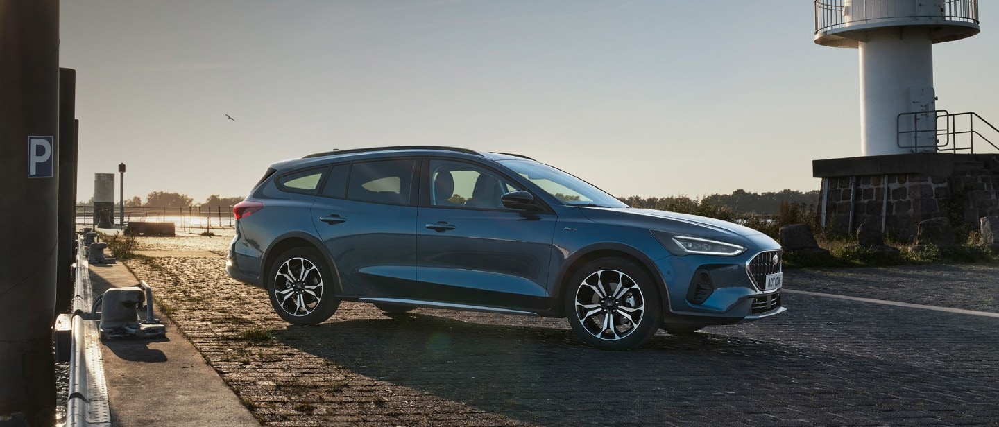 Ford Focus couleur bleue. Vue de face aux trois quarts, stationnant devant un lac.