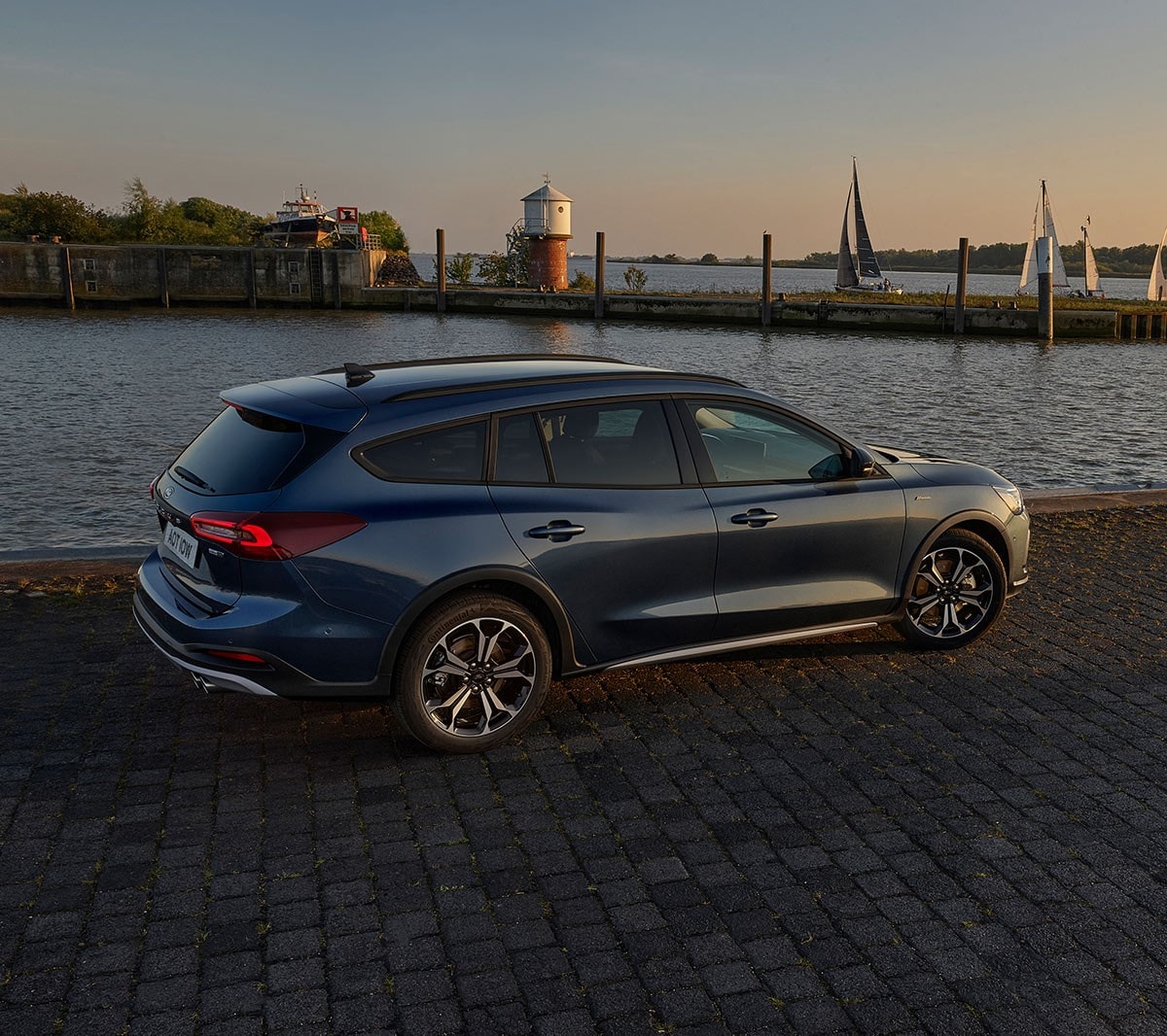 Ford Focus couleur bleue. Vue arrière aux trois quarts, garée devant un lac au coucher du soleil.
