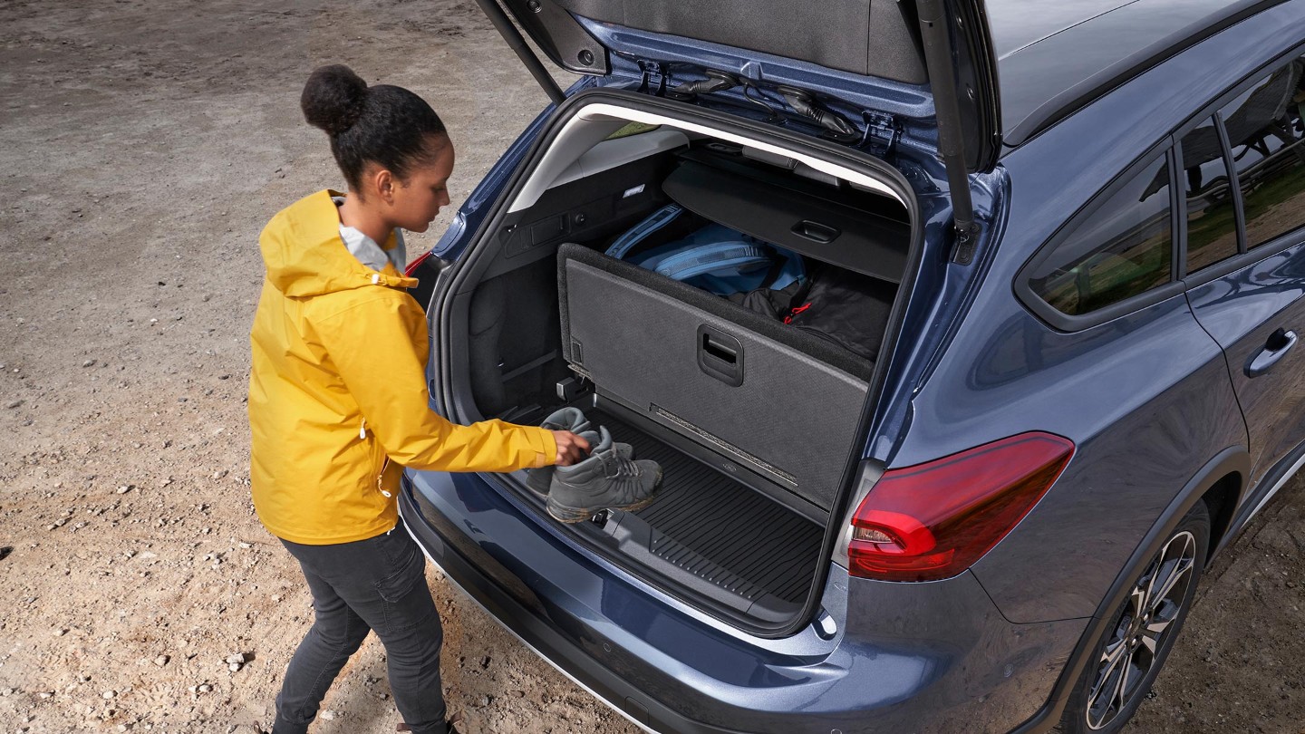 Ford Focus Active couleur bleue. Vue arrière aux trois quarts d’en haut. Une femme range des bagages dans le coffre.