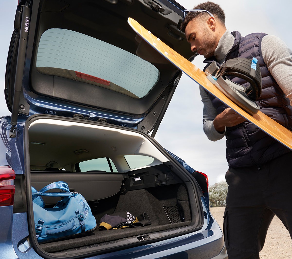 Ford Focus Active couleur bleue. Vue de trois quarts arrière, un homme range un snowboard dans le coffre.