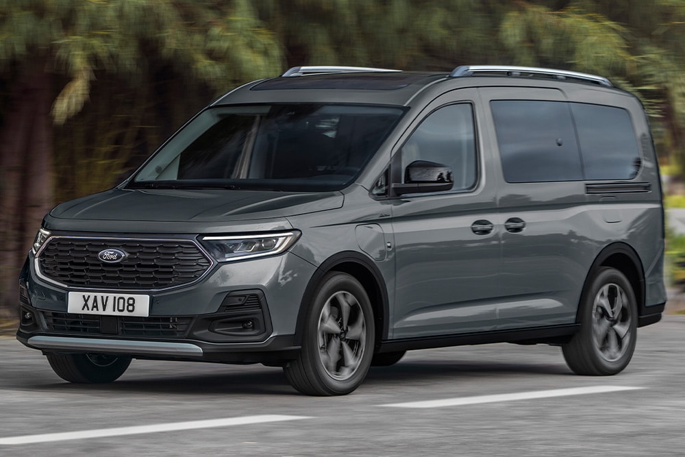 Ford Tourneo Connect couleur grise, vue de face aux trois quarts, roulant sur une route de montagne avec rivière en arrière-plan