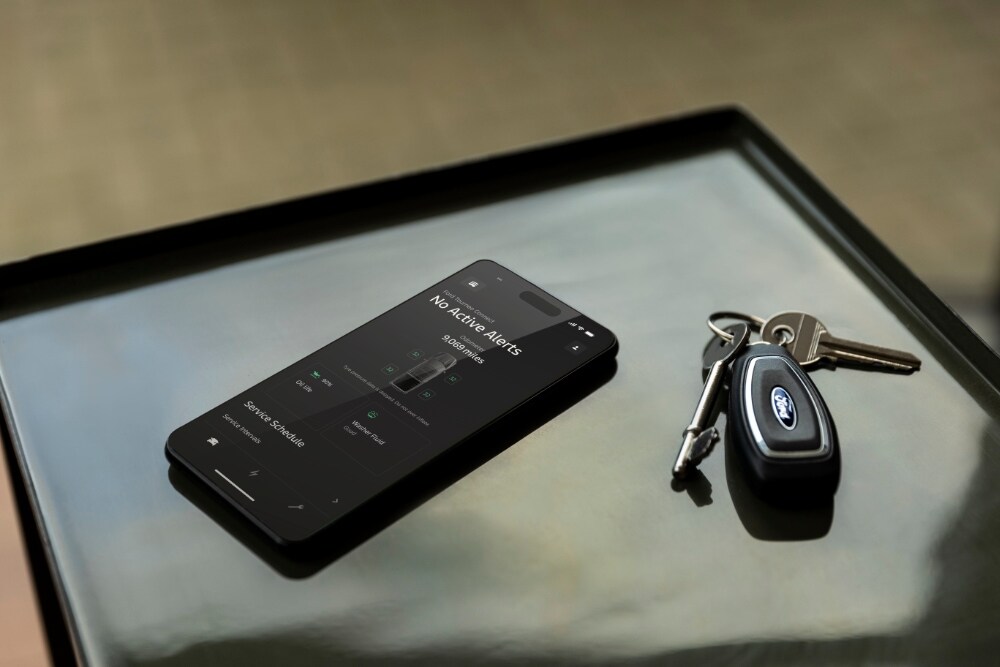 Un smartphone affiche l'application Ford avec le statut du véhicule, à côté d'une clé de voiture Ford.