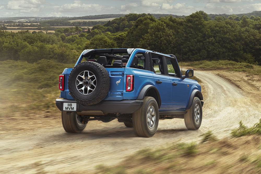 Vue arrière d'un Ford Bronco bleu traversant un paysage rural.