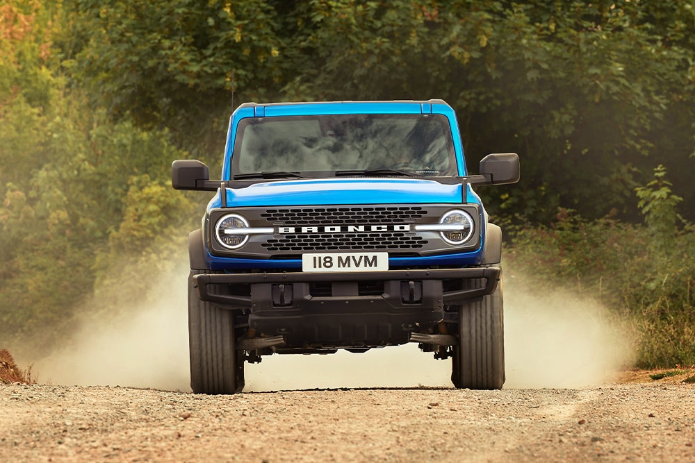Vue de face d'un Ford Bronco bleu roulant sur une route non goudronnée.