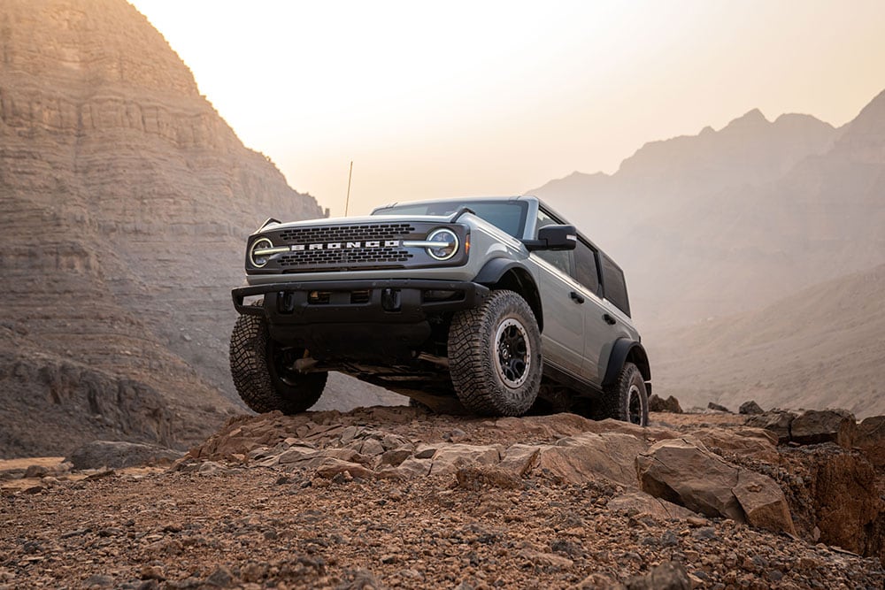 Un Ford Bronco gris stationné sur un sentier rocheux dans un décor de montagne.