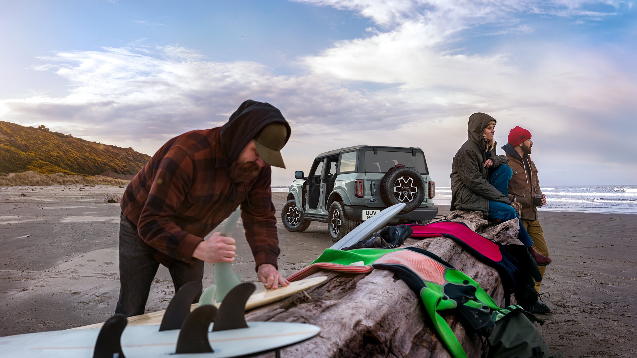 Ford Bronco couleur grise. Vue arrière aux trois quarts, garé devant un lac avec des personnes au premier plan.