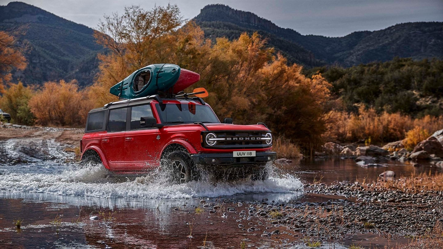 Ford Bronco en rouge, vue de face 3/4 dans un paysage rocheux traversant un cours d'eau