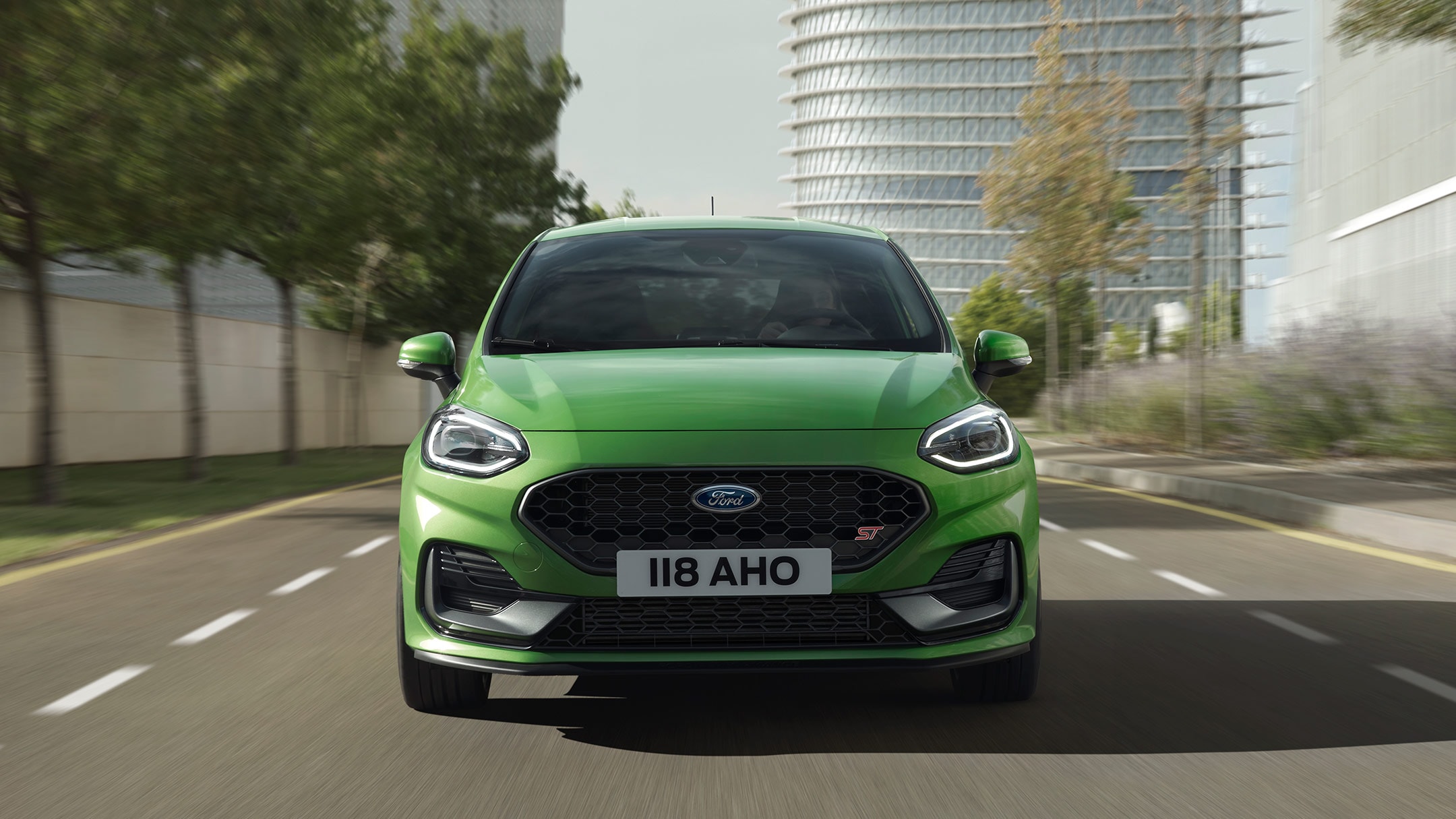 Ford Fiesta ST couleur verte. Vue de face sur une route devant des arbres et un bâtiment moderne.