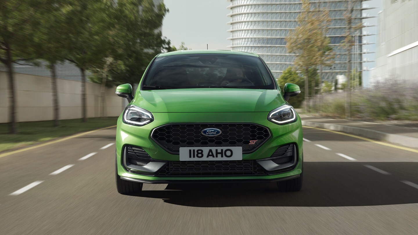 Ford Fiesta ST couleur verte. Vue de face sur une route devant des arbres et un bâtiment moderne.