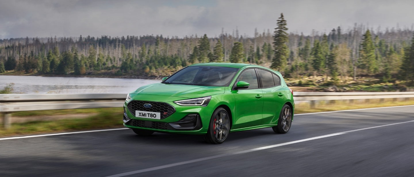 Ford Focus ST couleur verte. Vue de face aux trois quarts, roulant sur une route dans la forêt.