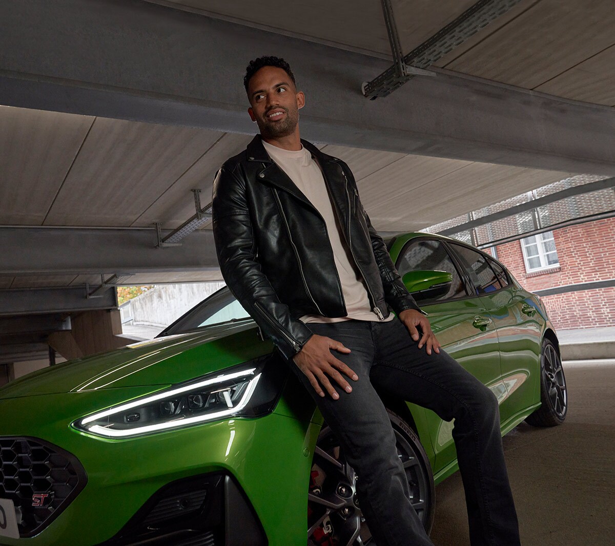 Homme adossé à la Ford Focus ST couleur verte. Vue de face aux trois quarts.