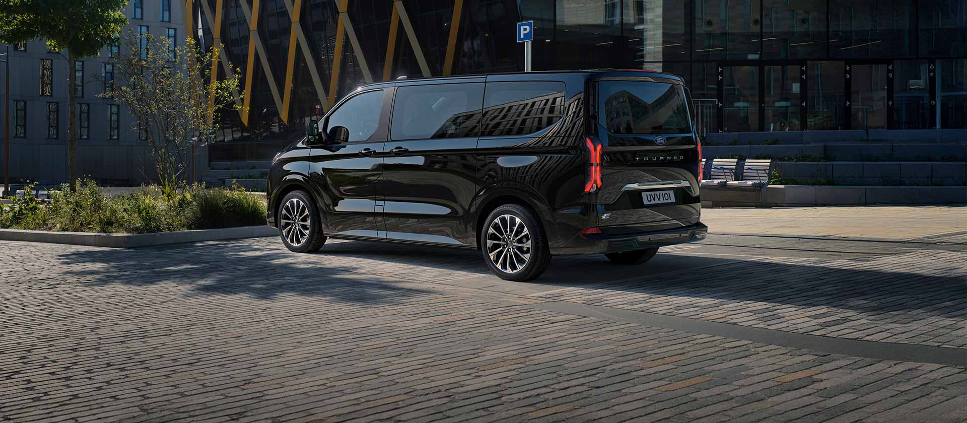 Ford E-Tourneo Custom noire, vue latérale et arrière devant un bâtiment moderne