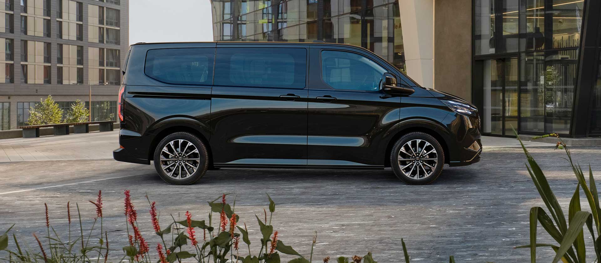 Ford E-Tourneo Custom noir garé devant un bâtiment moderne.