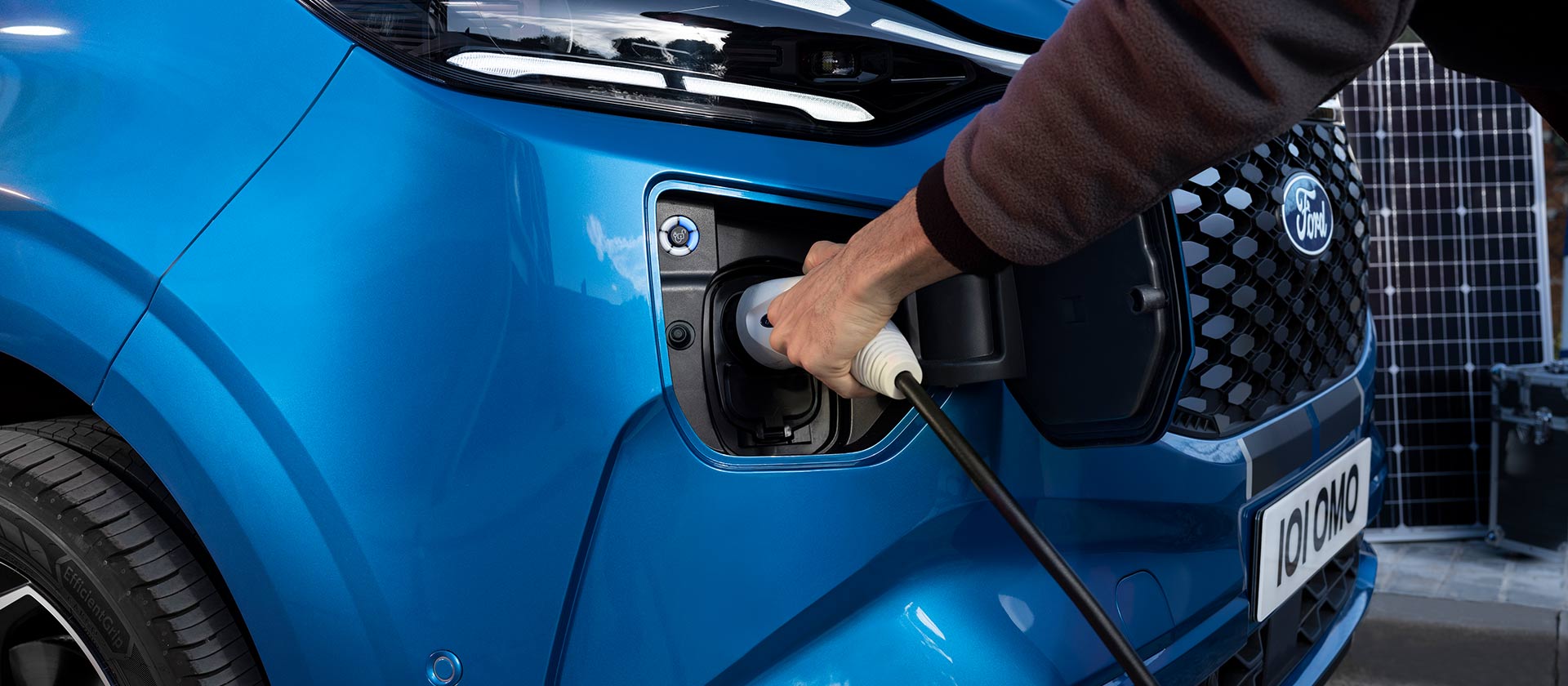 Une main branche le câble de recharge dans la Ford E-Tourneo Custom bleue