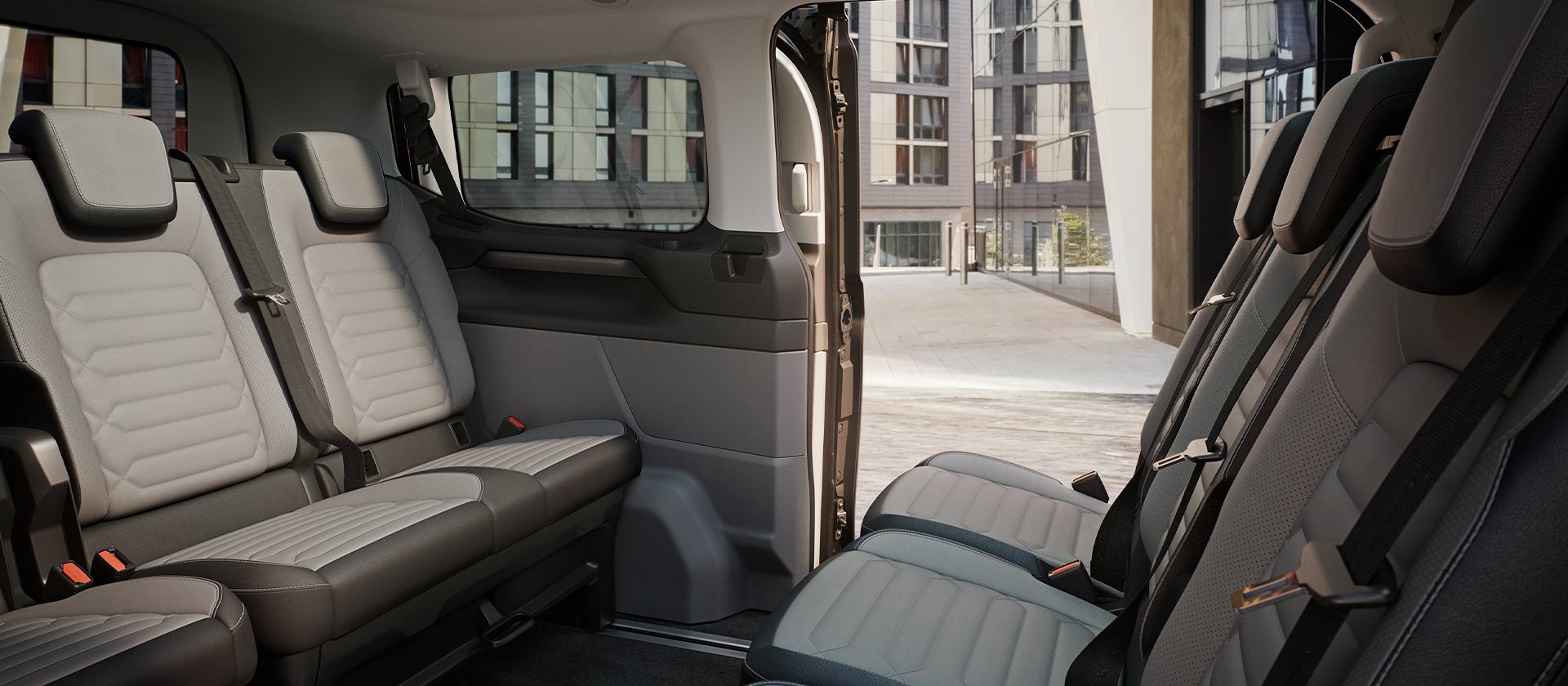 Vue intérieure du Ford Tourneo Custom avec plusieurs rangées de sièges gris et toit panoramique