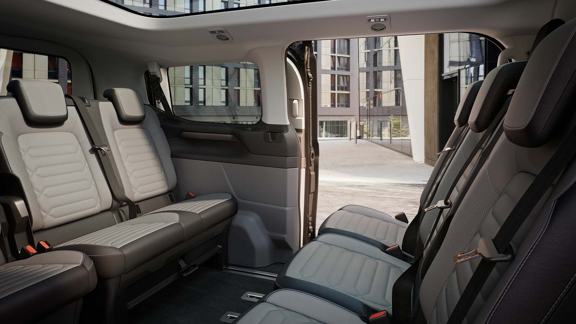 Vue intérieure du Ford Tourneo Custom avec plusieurs rangées de sièges gris et toit panoramique